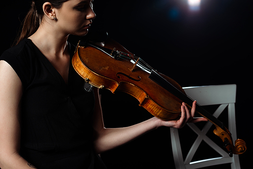 beautiful female musician playing on violin on black with back light