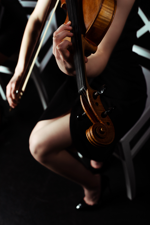 cropped view of female musician playing on violin on dark stage