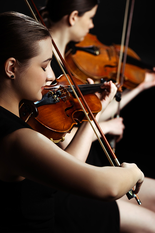 professional female musicians playing classical music on violins on dark stage, selective focus
