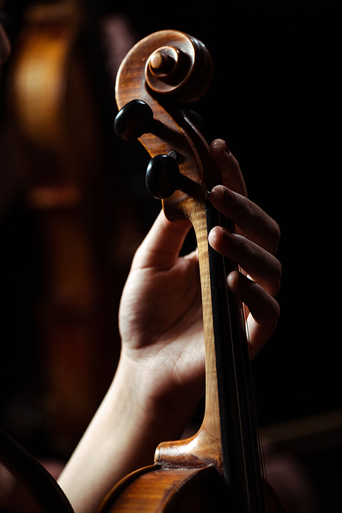 cropped view of female musician playing on violin on dark stage