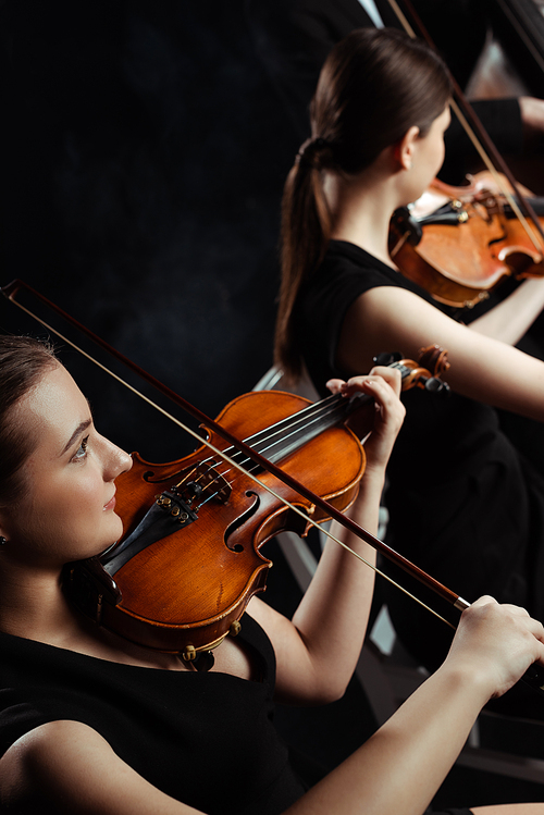 young professional musicians playing classical music on violins on dark stage