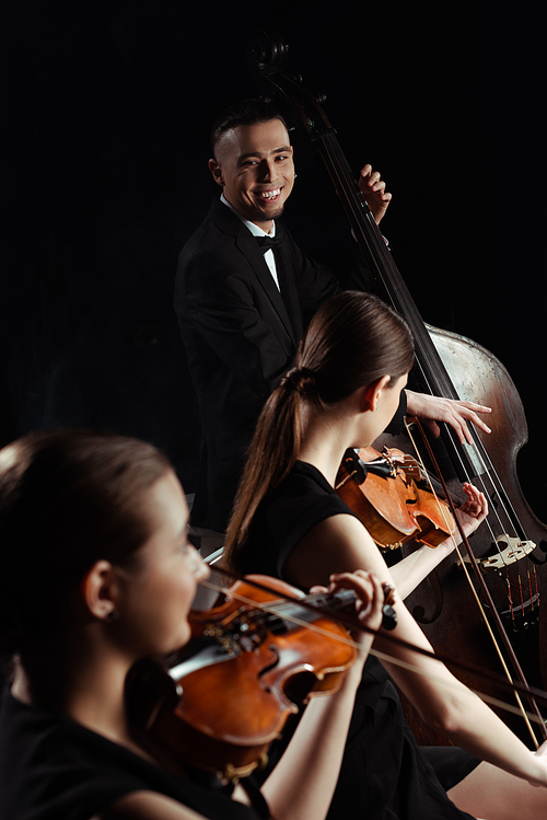 happy professional musicians playing on double bass and violins isolated on black