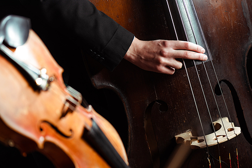 professional musician playing on double bass on dark stage with selective focus of violin