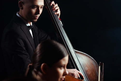 professional musicians playing on violin and contrabass on dark stage