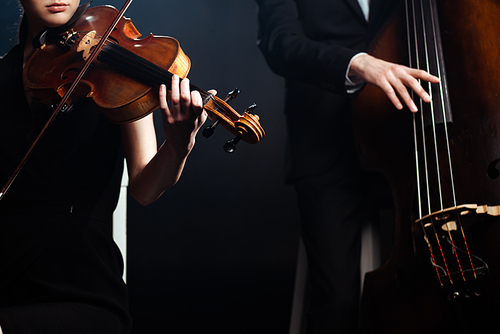 cropped view of professional musicians playing on violin and contrabass on dark stage