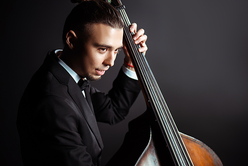 young professional musician playing on double bass on dark stage
