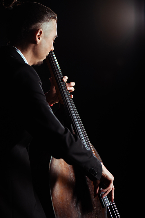 professional young musician playing on contrabass on dark stage