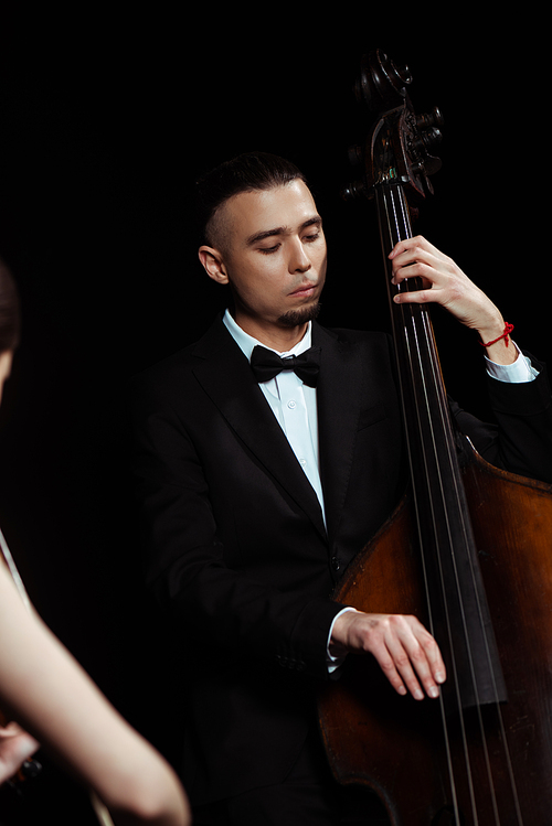 focused professional musicians playing on violin and contrabass on dark stage