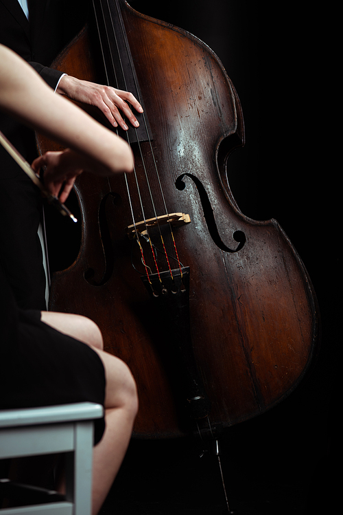 cropped view of professional musicians playing classical music on violin and contrabass on dark stage
