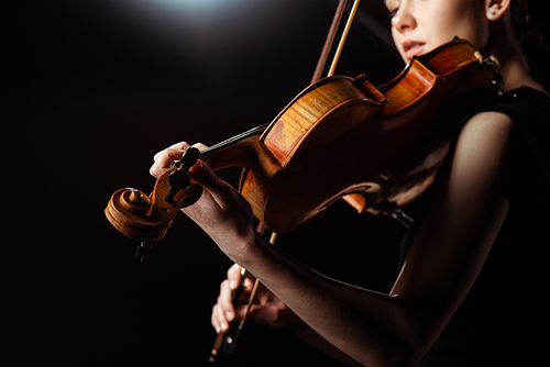 attractive female musician playing on violin on dark stage