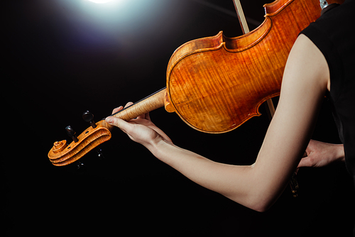cropped view of professional female musician playing on violin on dark stage