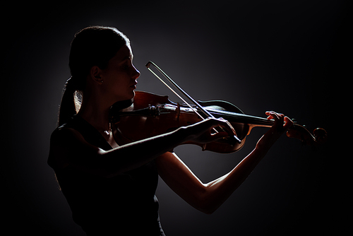 silhouette of professional musician playing on violin on dark stage
