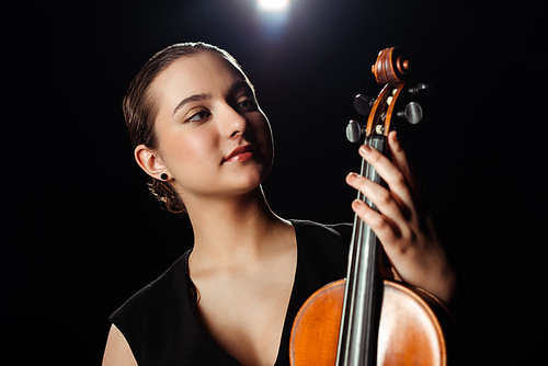 attractive female musician playing on violin on black with backlit