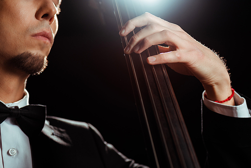 cropped view of musician playing on contrabass on dark stage with back light
