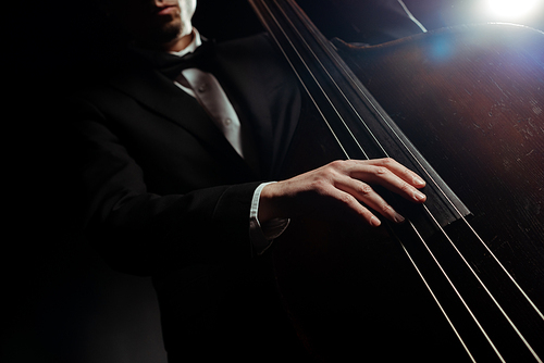 cropped view of musician playing on double bass on dark stage