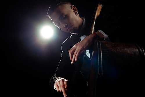 professional musician playing on double bass on dark stage with back light