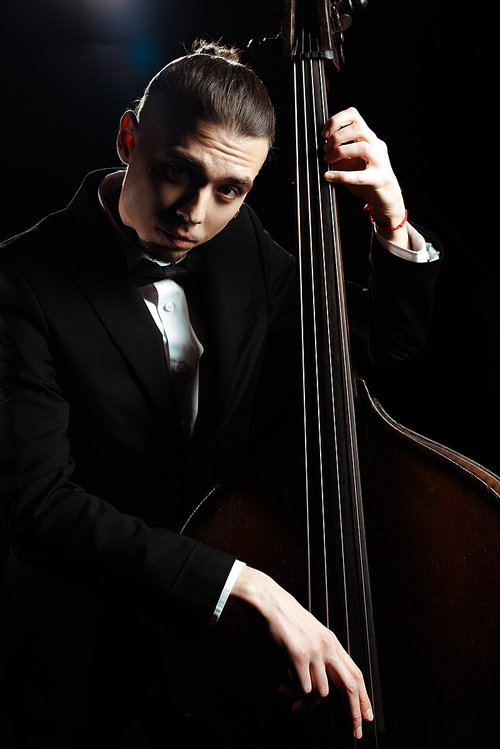 professional musician playing on double bass on dark stage