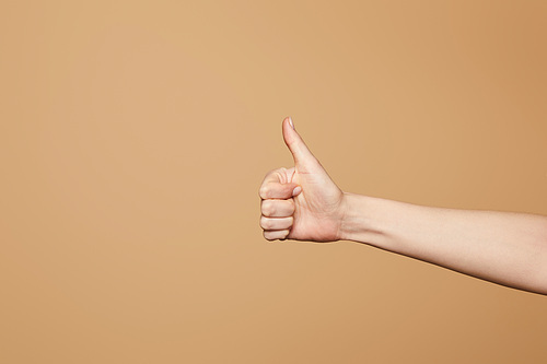 cropped view of woman showing thumb up isolated on beige