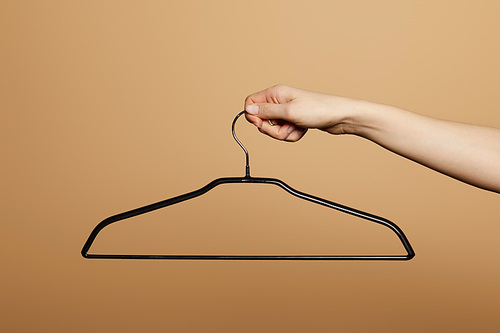 cropped view of woman holding empty hanger isolated on beige