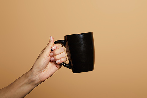 cropped view of woman holding black mug isolated on beige