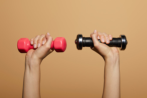 cropped view of woman holding dumbbells isolated on beige