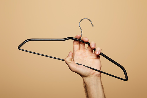 cropped view of man holding empty hanger isolated on beige