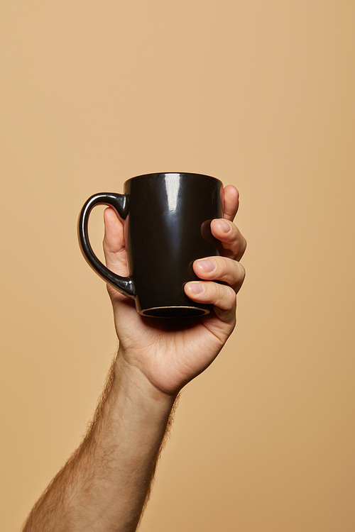 cropped view of man holding black mug isolated on beige