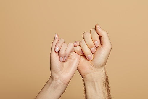 cropped view of man and woman holding little fingers isolated on beige