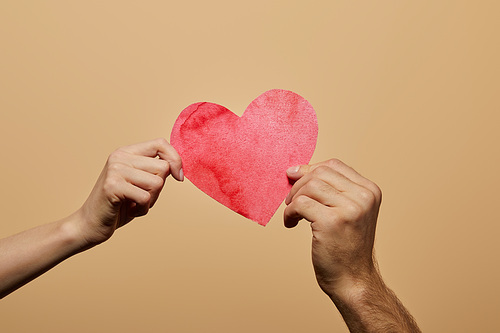 cropped view of man and woman holding red heart isolated on beige