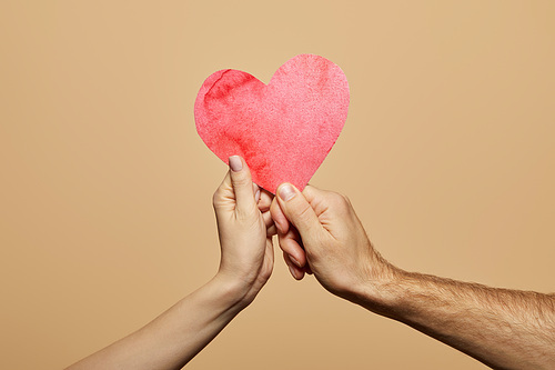 cropped view of man and woman holding red heart isolated on beige