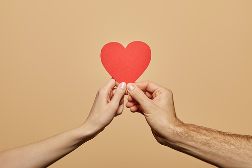 cropped view of man and woman holding red heart isolated on beige