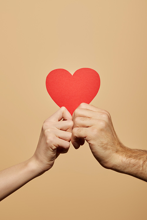 cropped view of man and woman holding red heart isolated on beige