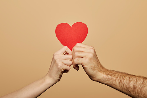 cropped view of man and woman holding red heart isolated on beige