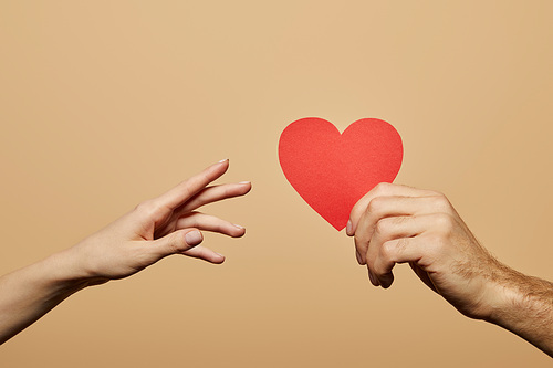 cropped view of man holding red heart and woman reaching it isolated on beige