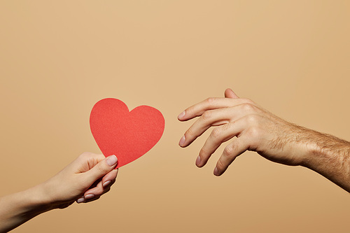 cropped view of woman holding red heart and man reaching it isolated on beige