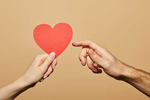 cropped view of woman holding red heart and man reaching it isolated on beige