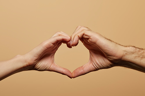 cropped view of man and woman showing heart gesture isolated on beige