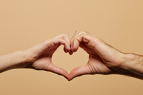 cropped view of man and woman showing heart gesture isolated on beige