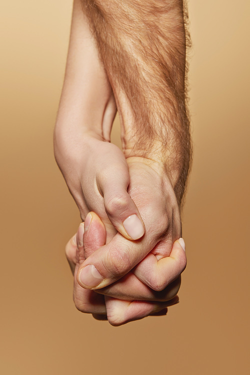 partial view of man and woman firmly holding hands isolated on beige