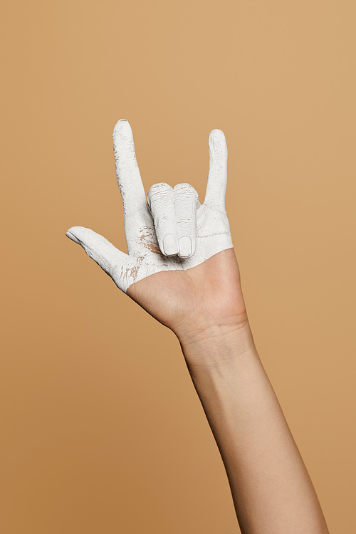 cropped view of woman with white painted hand showing rock gesture isolated on beige