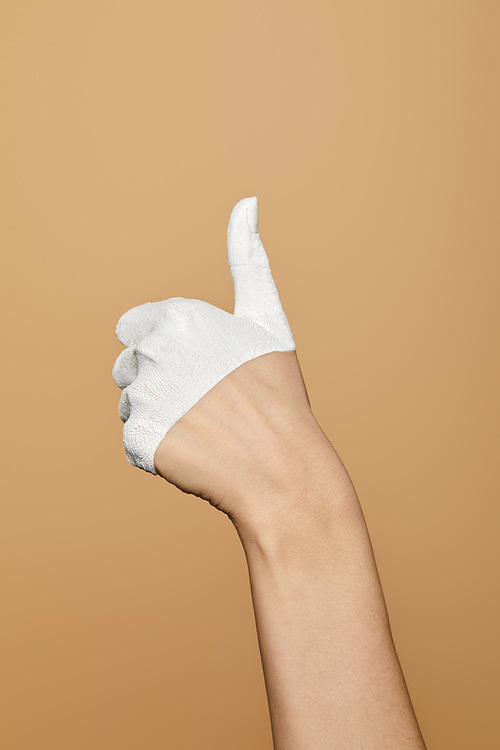 cropped view of woman with white painted hand showing thumb up isolated on beige