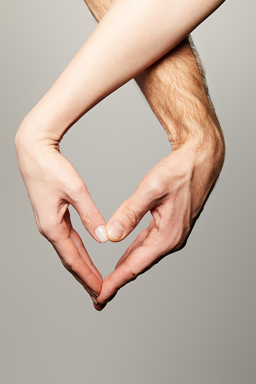 cropped view of man and woman showing heart gesture isolated on grey