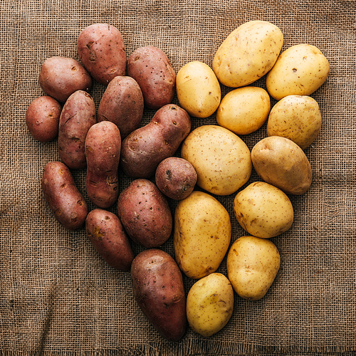 top view of organic raw potatoes arranged in heart on brown rustic sackcloth