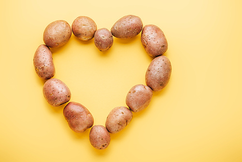 top view of raw whole fresh potatoes arranged in heart on yellow background