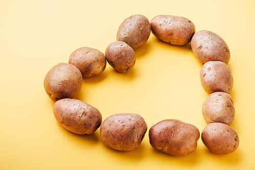 raw whole fresh potatoes arranged in heart on yellow background