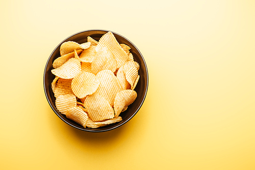 top view of delicious crispy potato chips in bowl on yellow background