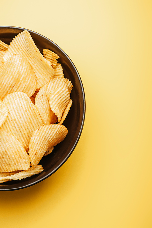 top view of delicious crispy potato chips in bowl on yellow background