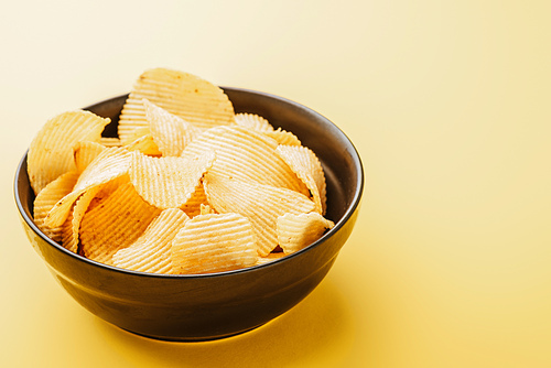 delicious crispy potato chips in bowl on yellow background