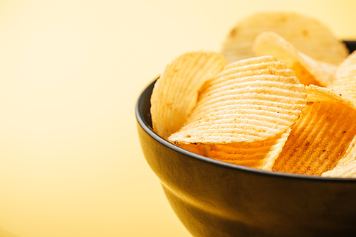 close up view of delicious crispy potato chips in bowl on yellow background