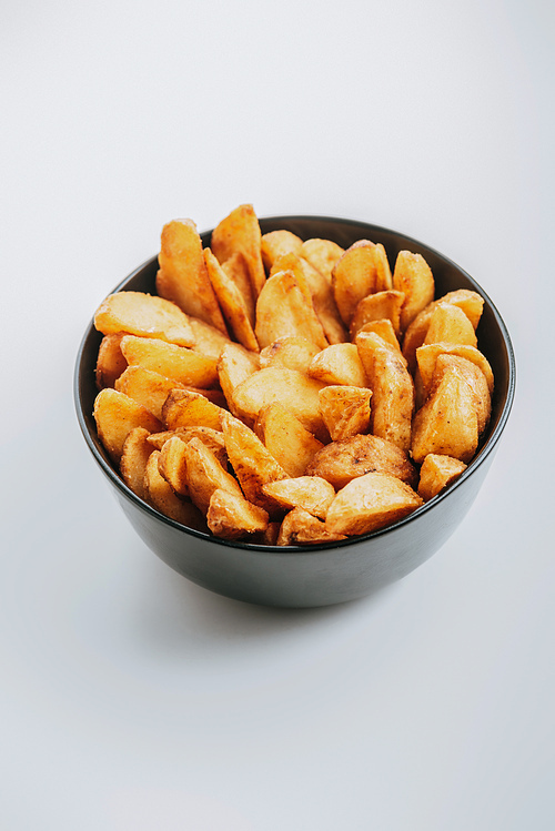 delicious golden potato wedges in bowl on grey background